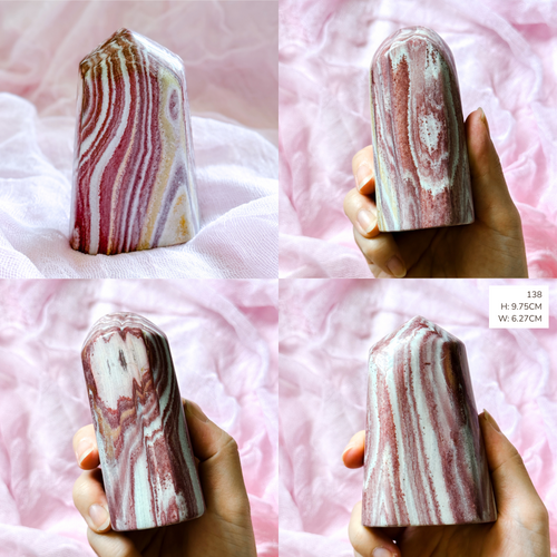 Marble-patterned cylindrical picture jasper freeform held by hands on a pink textured background